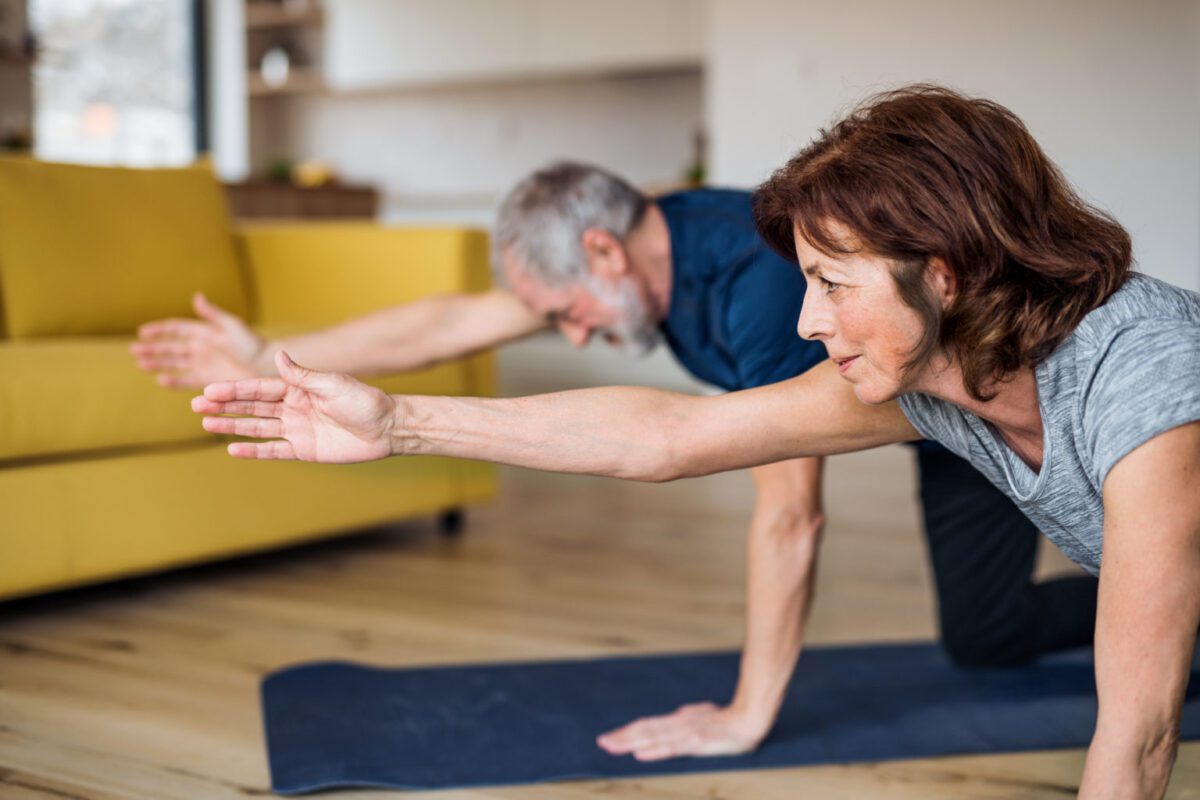 A senior couple indoors at home, doing exercise on the floor.