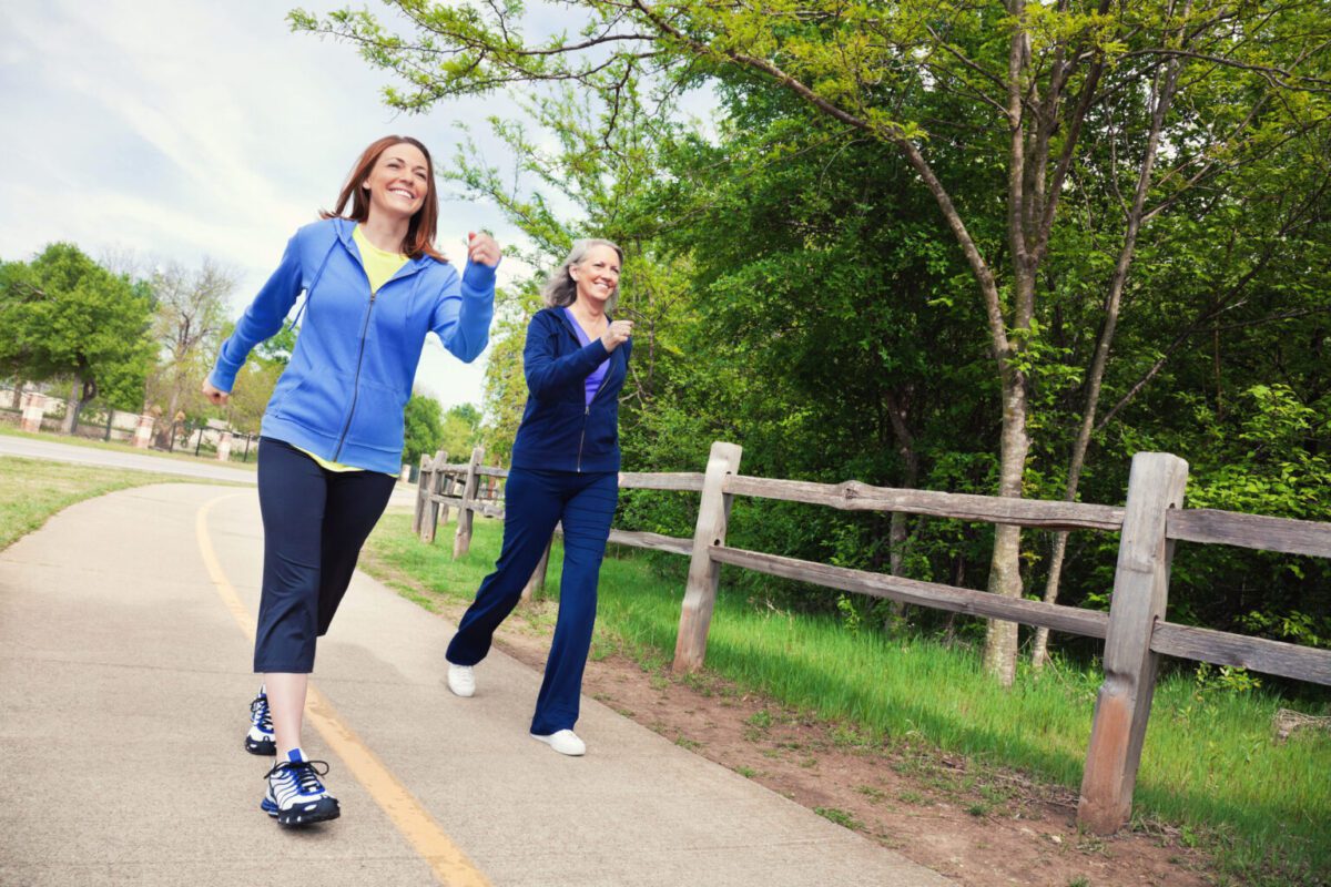 Woman power walks at park with senior mom