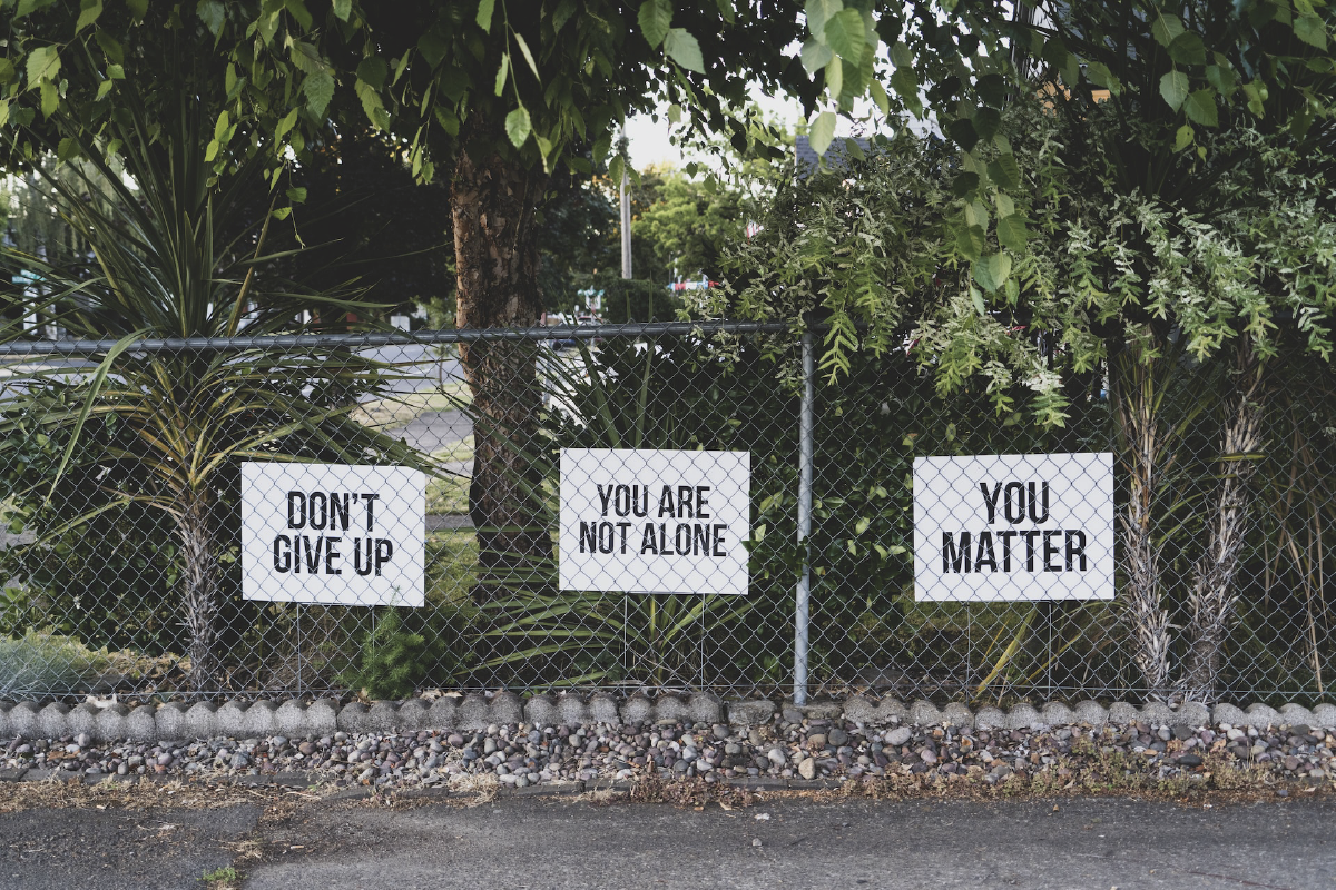 Encouraging signs on a fence, that say Don't Give Up, You Are Not Alone, You Matter