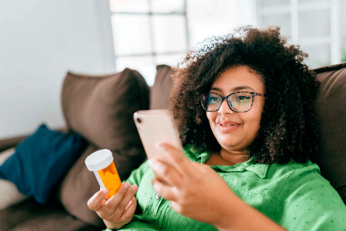 Woman with a prescription bottle in her hand and looking at her phone.