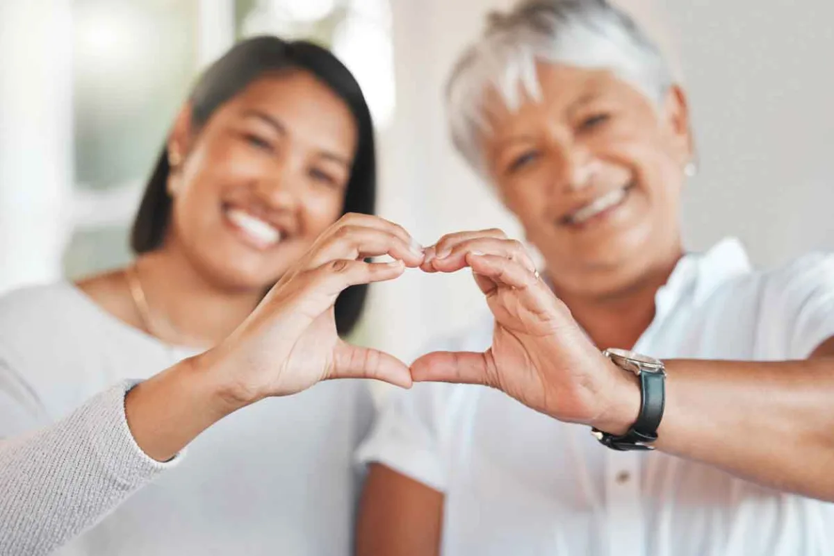 Two women each using one hand to form heart with their fingers touching