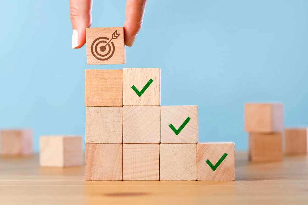 Hand stacking small wooden blocks. Top block has a bullseye graphic on it.