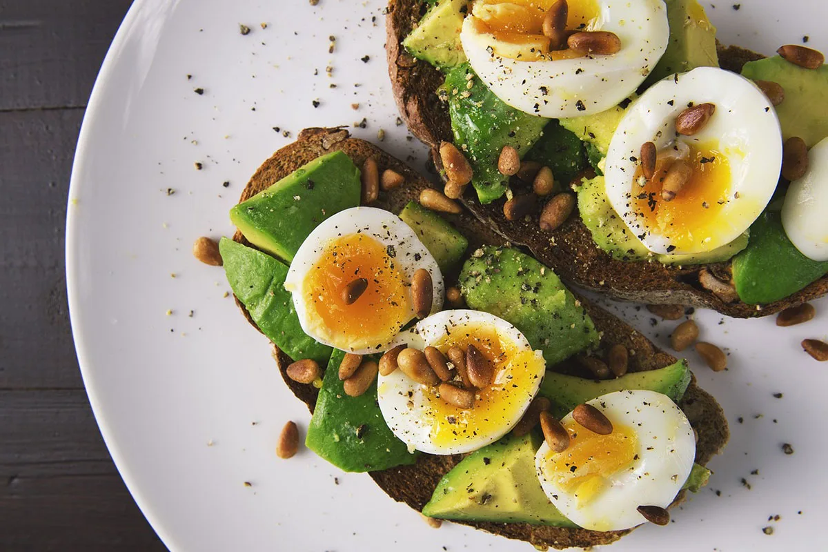 two pieces of avocado toast with hard boiled egg, pine nuts and pepper