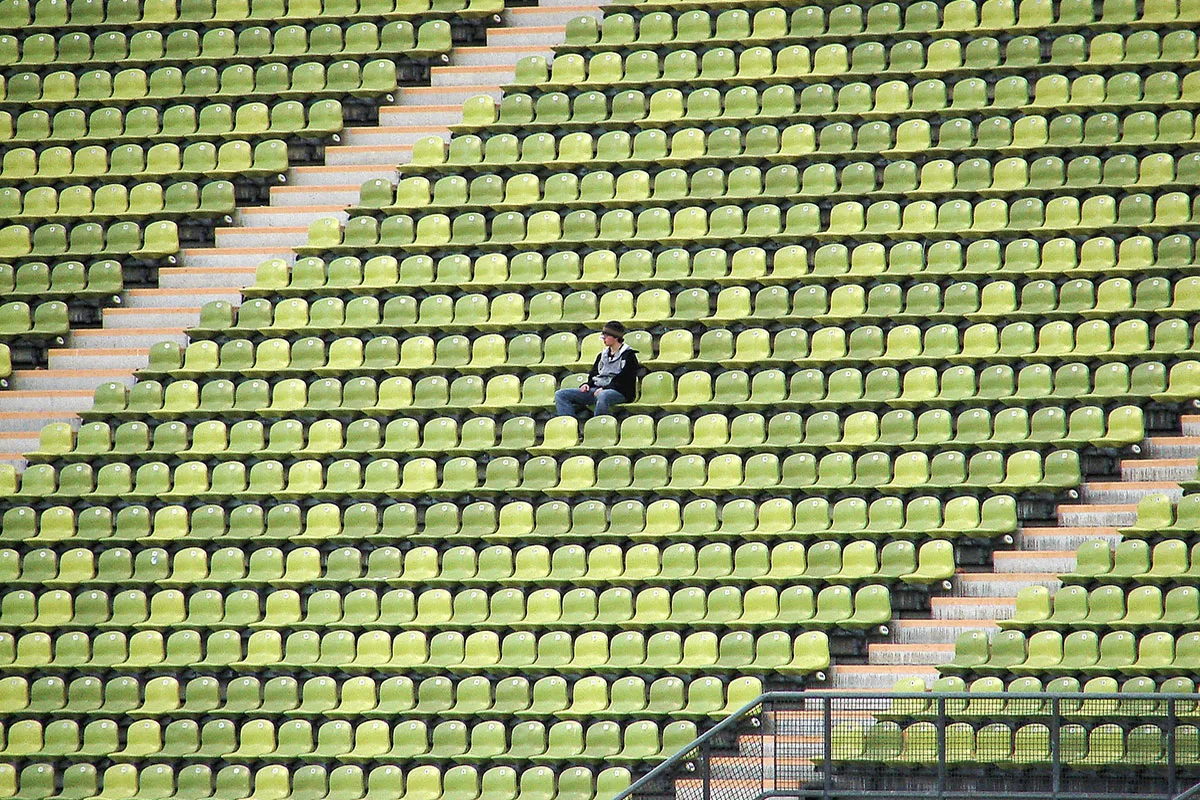 Person sitting alone in a large empty section of a stadium
